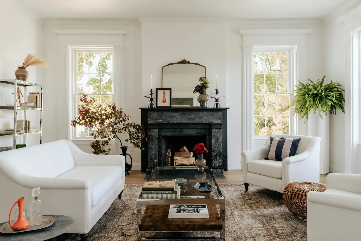 Bright traditional living room with black marble fireplace, gilded mirror, white sofas and tall windows